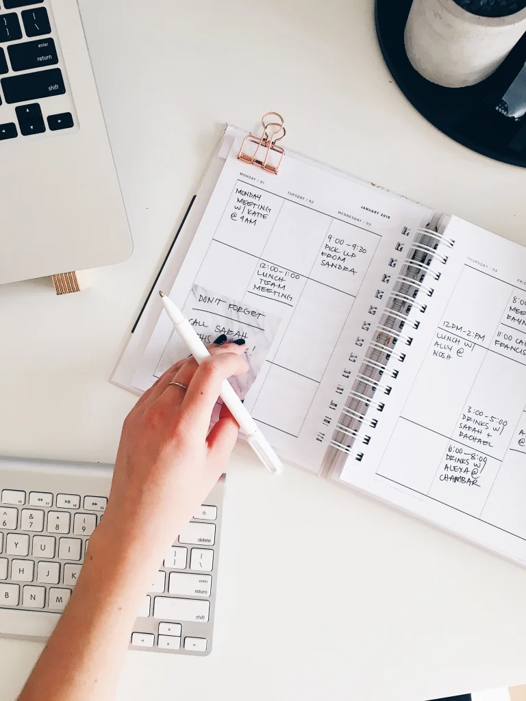 Hand met pen bij een weekplanning in een notitieboek op een bureau